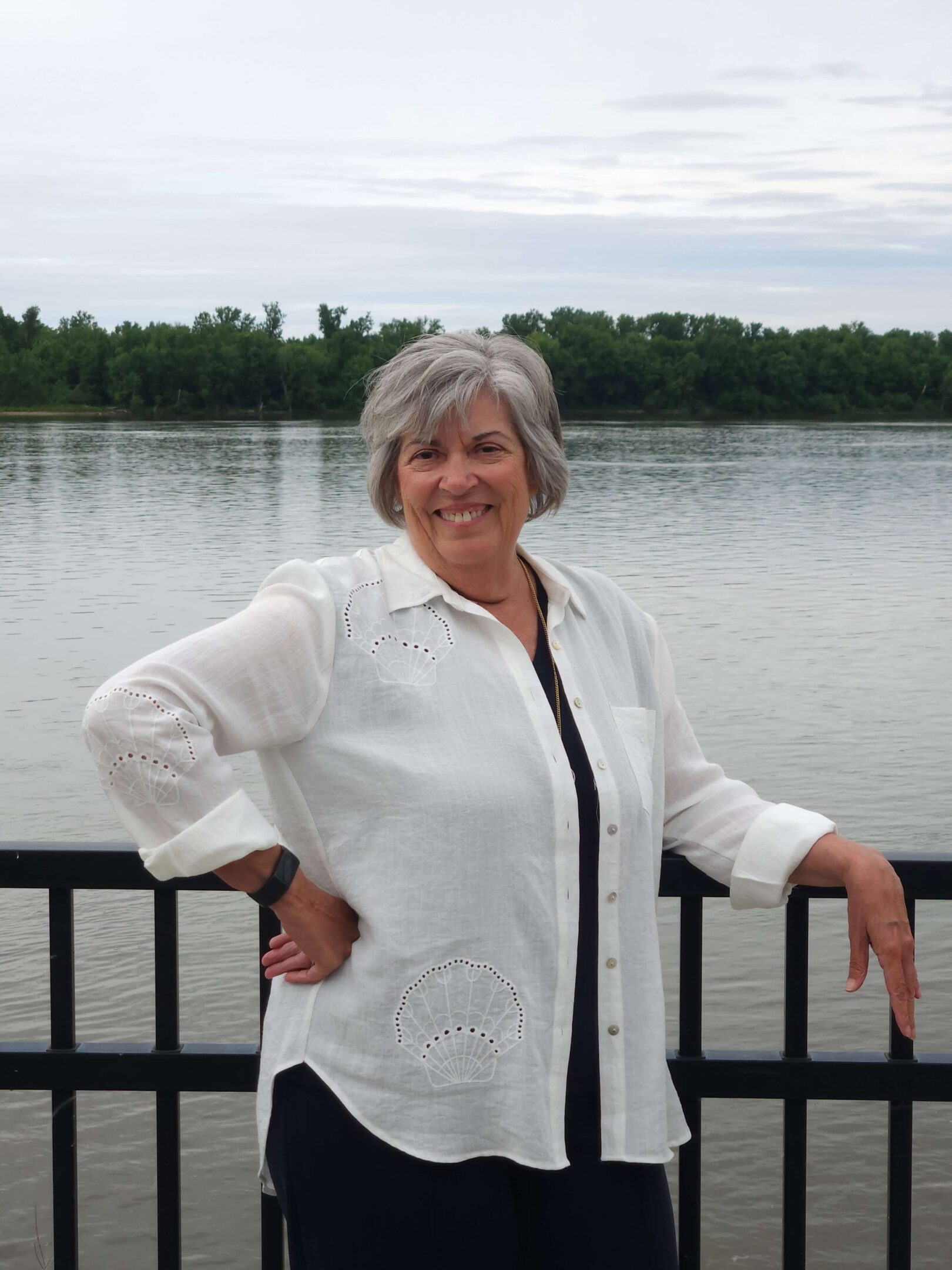 Smiling woman standing by a lakeside railing.