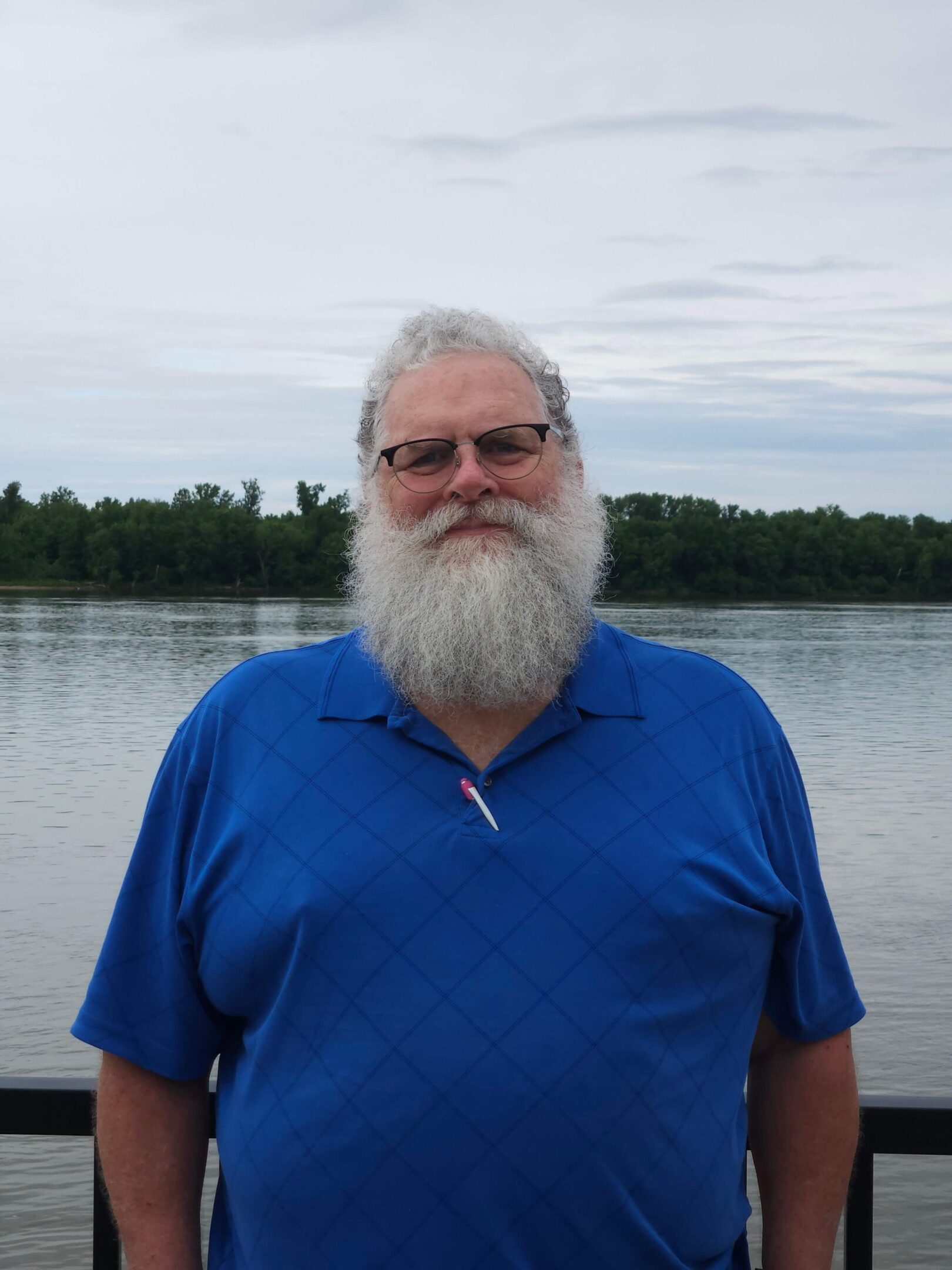 Man with beard standing by a river.