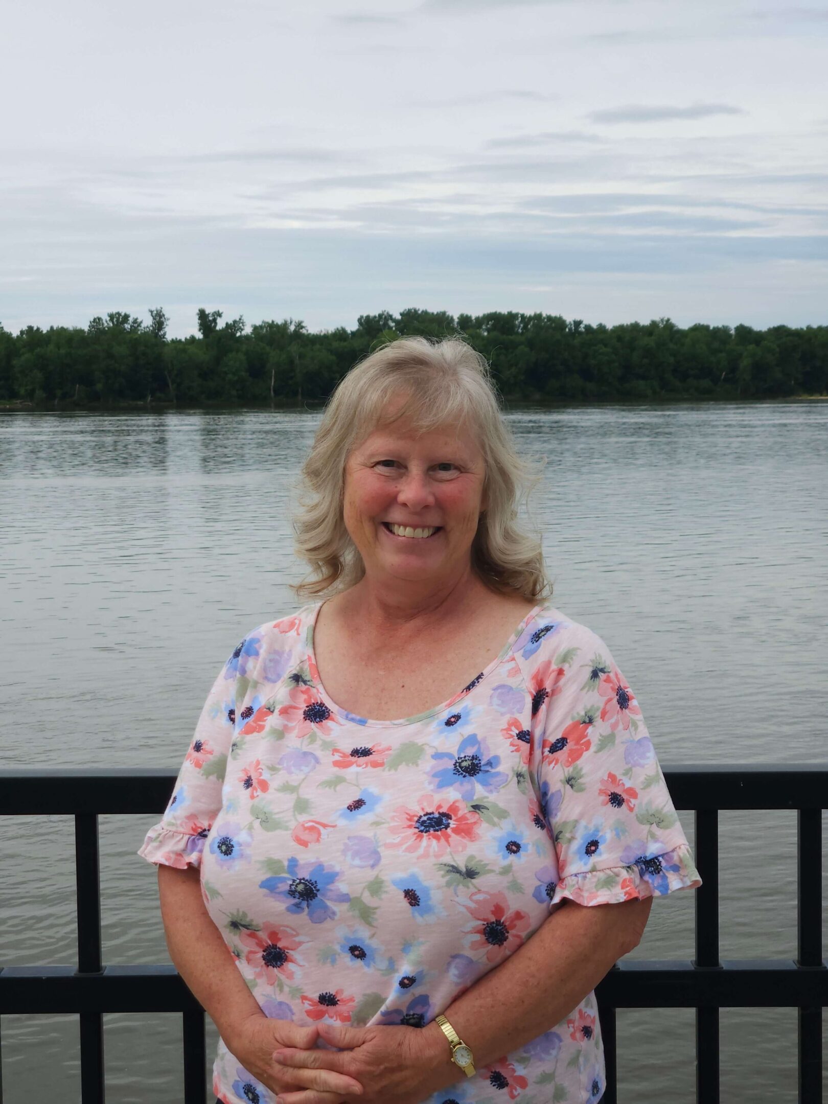 Smiling woman by a riverside railing.