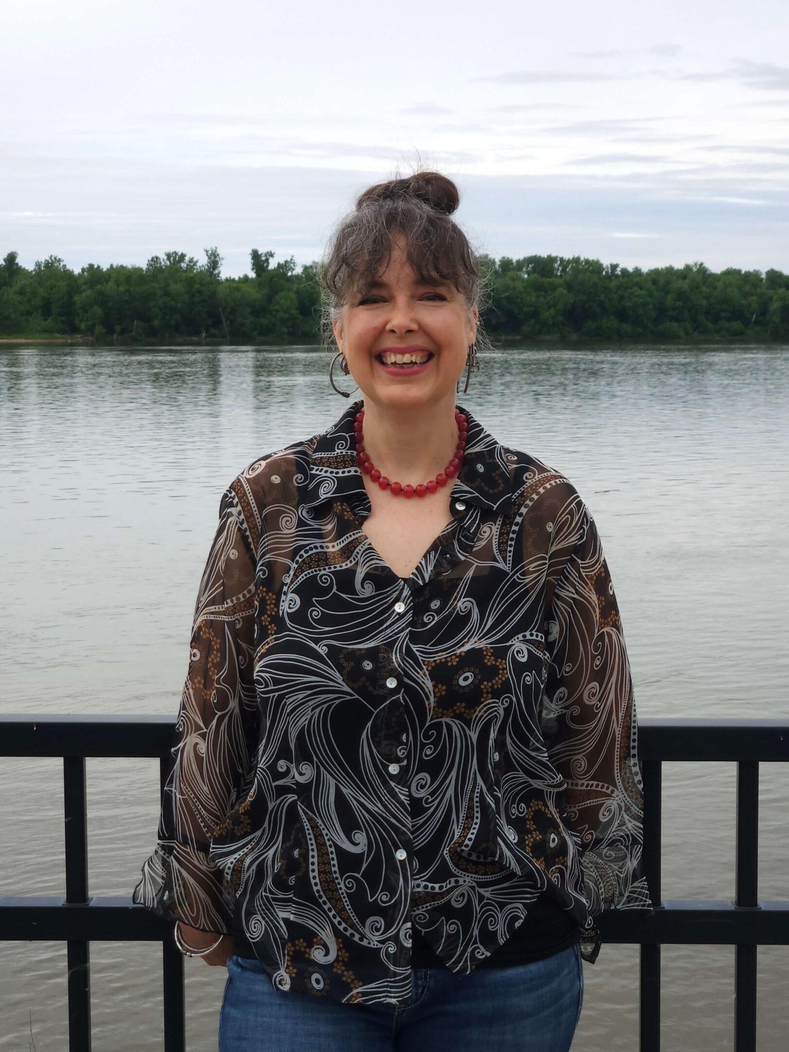 Smiling person standing by a riverside railing.