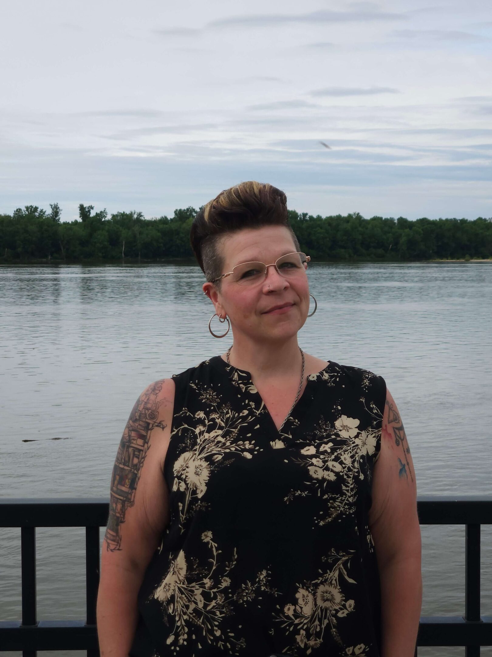 Person standing by a lake, cloudy sky.